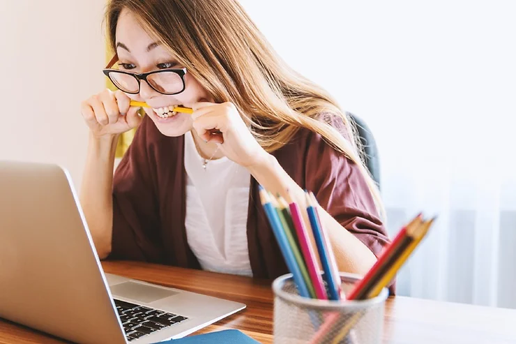 a woman feeling flustered looking at her laptop while biting down on a pencil to relieve stress and frustration